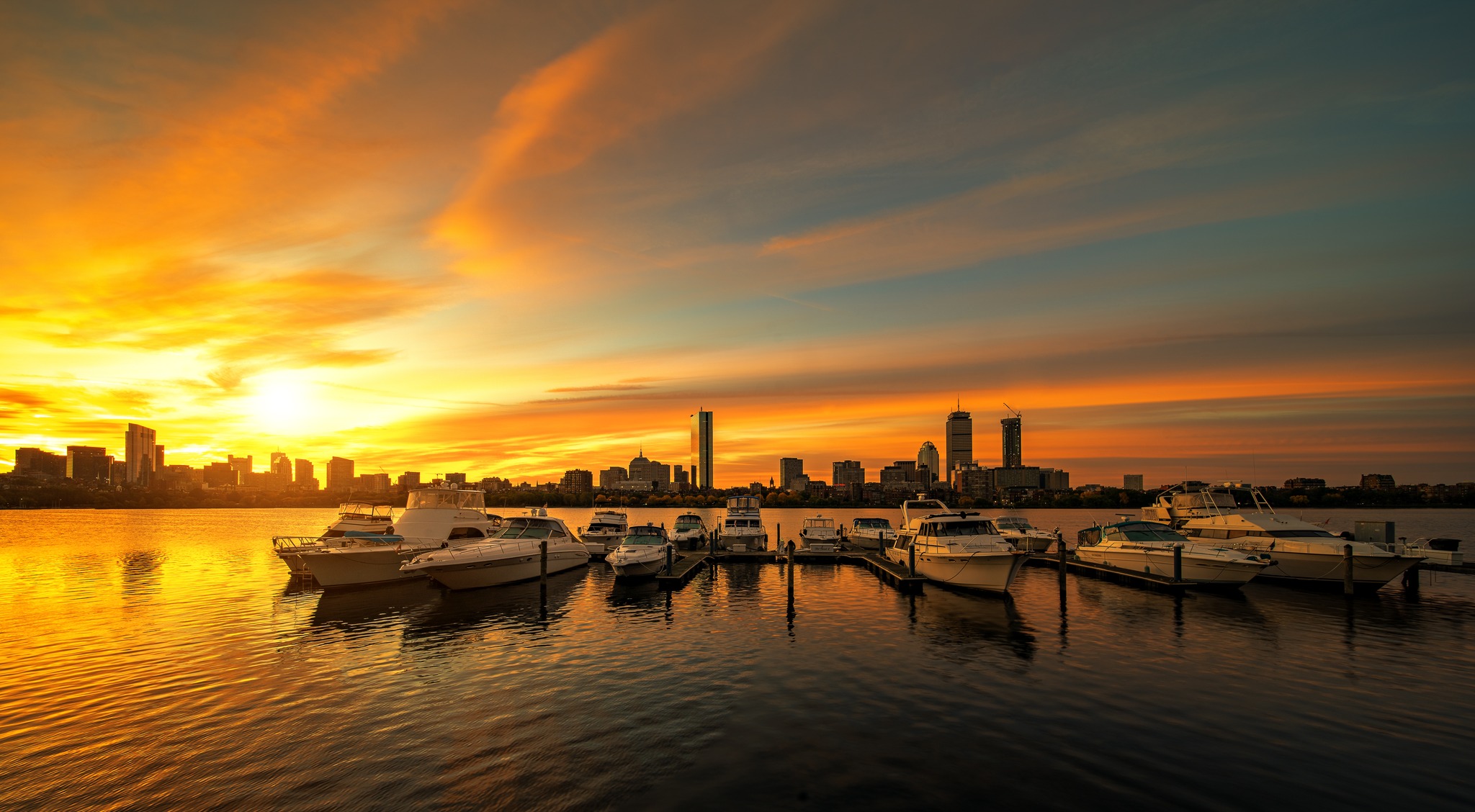 A calm waterfront city at sunset with boats at a dock, warm light fading into open sky, suggesting reflection and reduction.