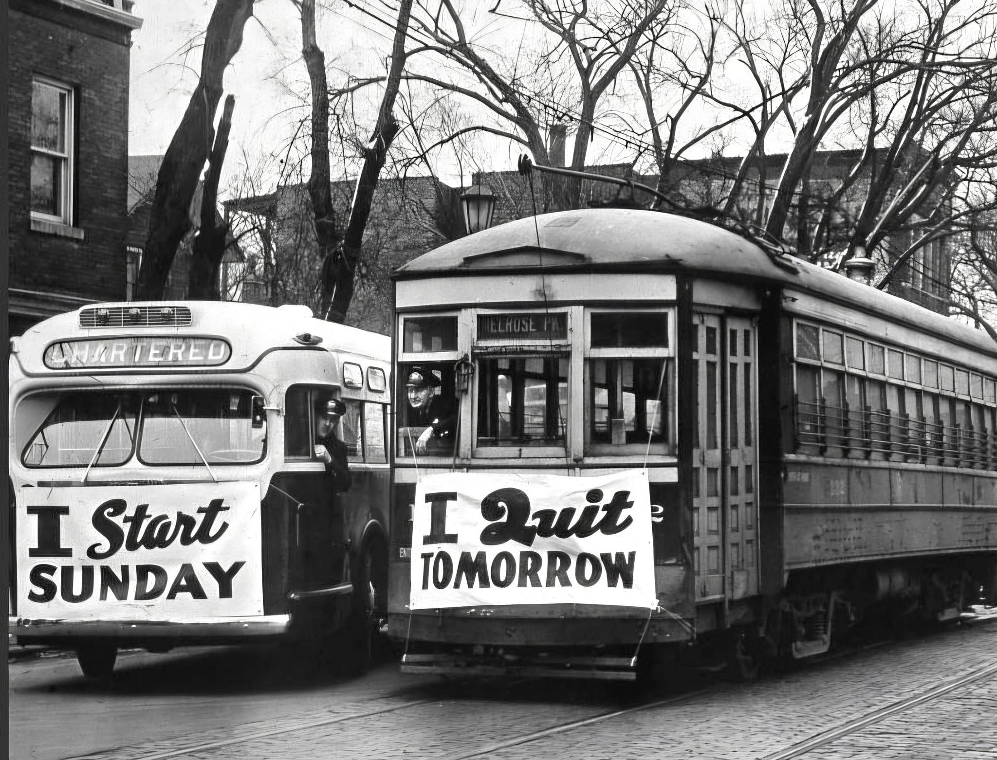 Black-and-white photo of two vintage transit vehicles side by side, one reading 'I Start Sunday' and the other 'I Quit Tomorrow,' suggesting the quiet deferral of change