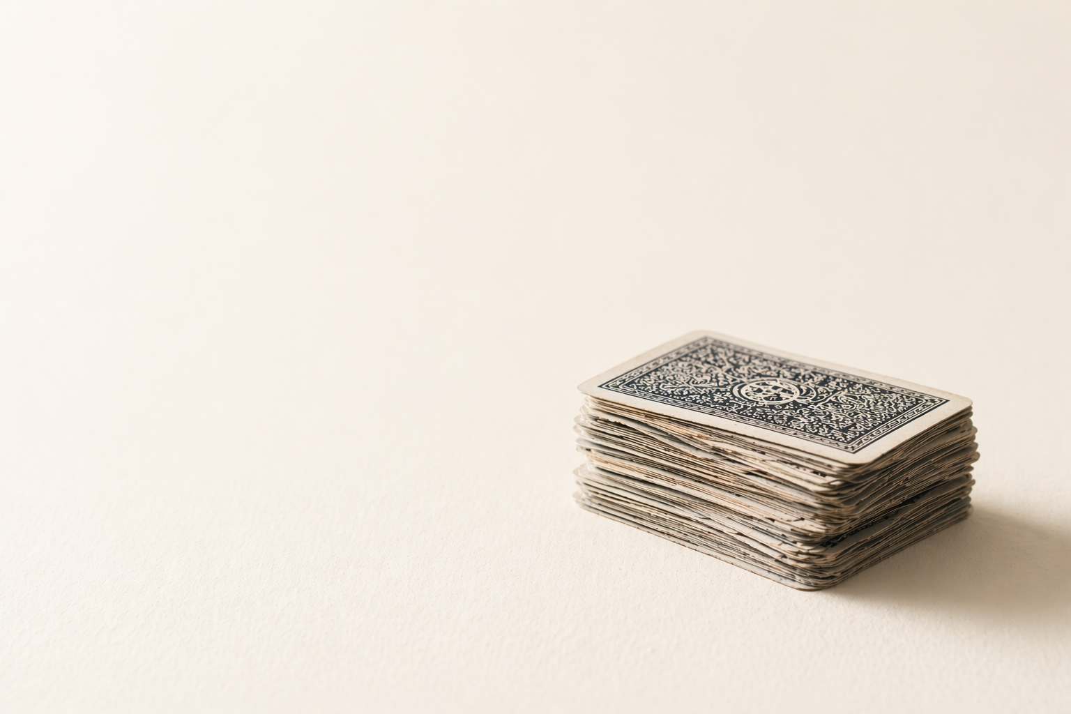 A minimal, text-free composition of a slightly imperfect stack of playing cards on a warm off-white surface, softly lit with shallow depth of field.